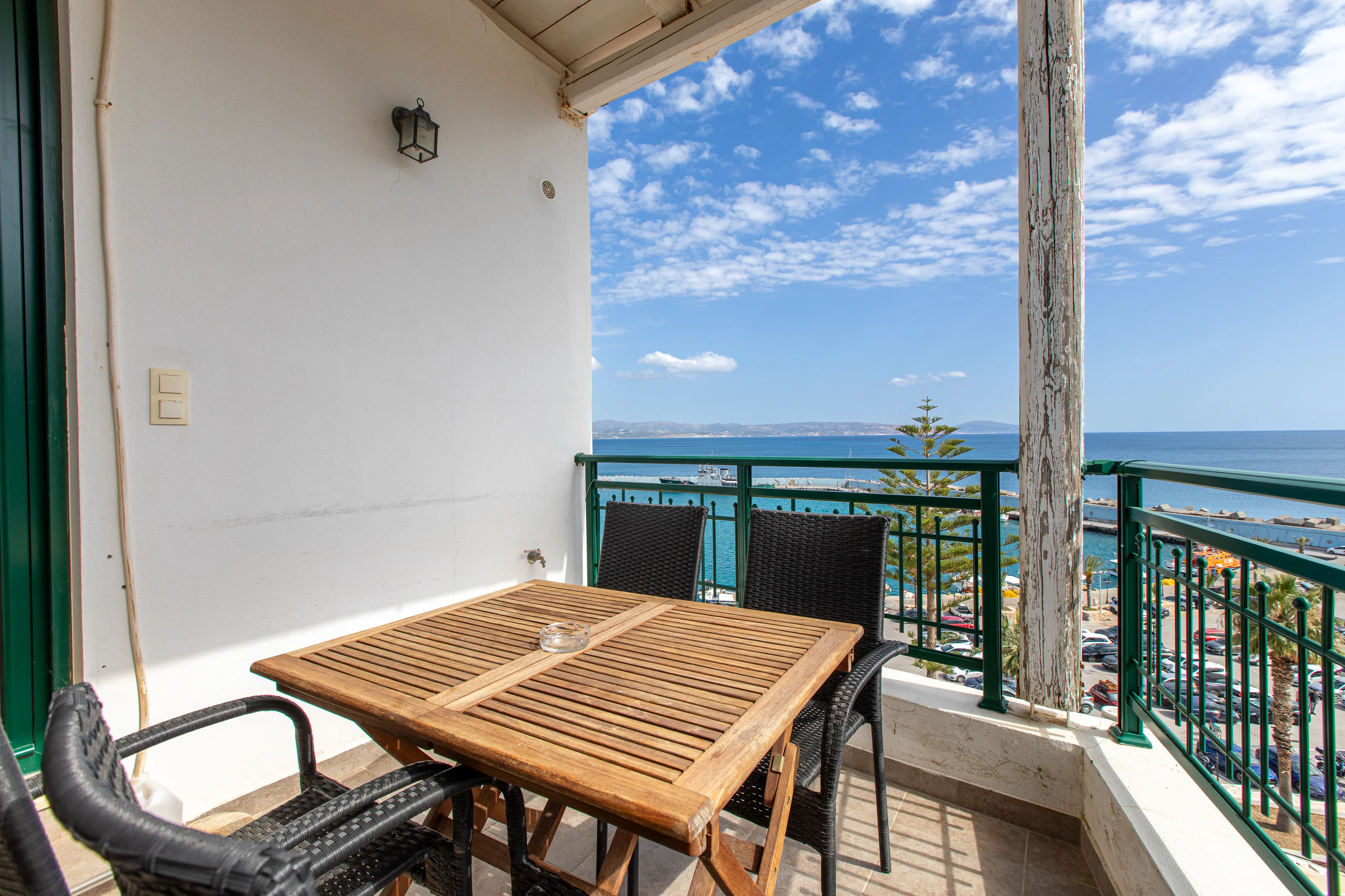 outside view of the apartment's balcony with a wooden table with armchairs and the view of the sea at the background