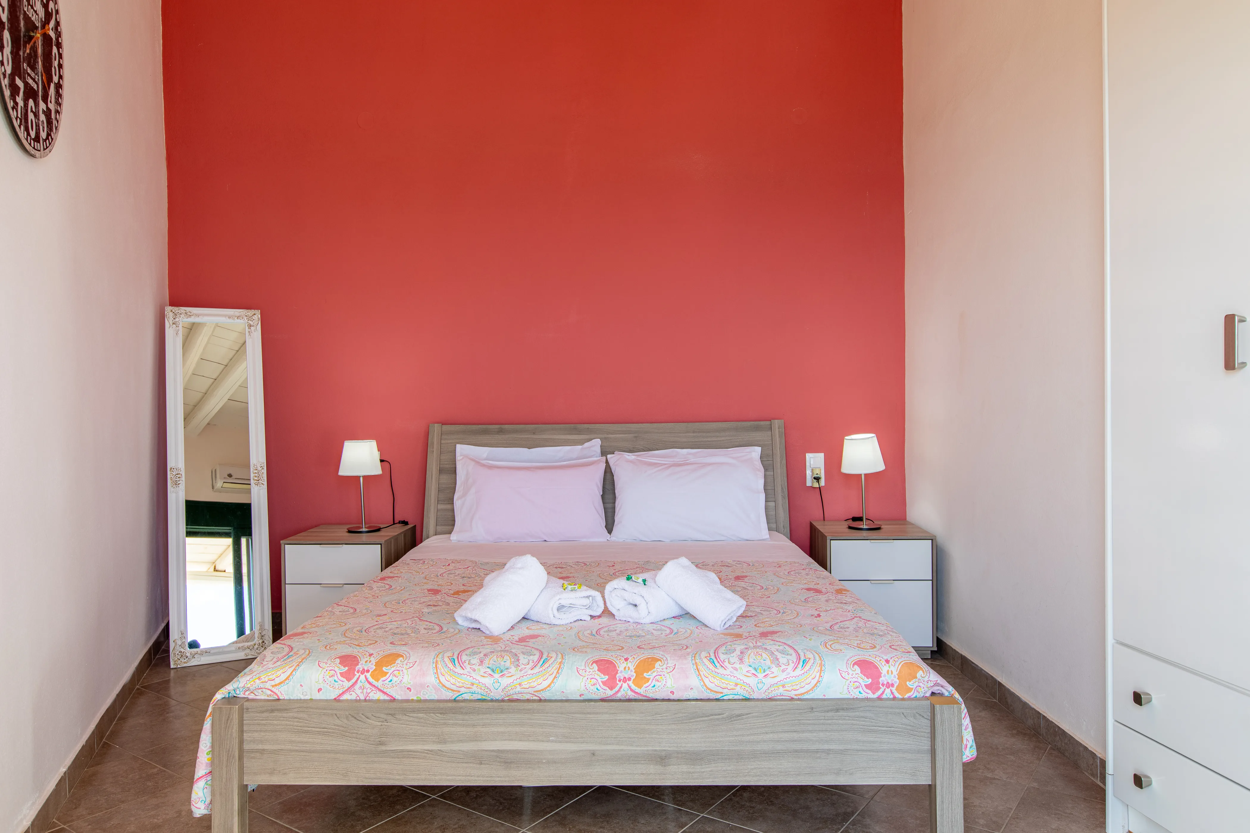 inside view of the apartment room featuring a large double bed from the front side with a red painted wall behind it and a floor mirror next to it