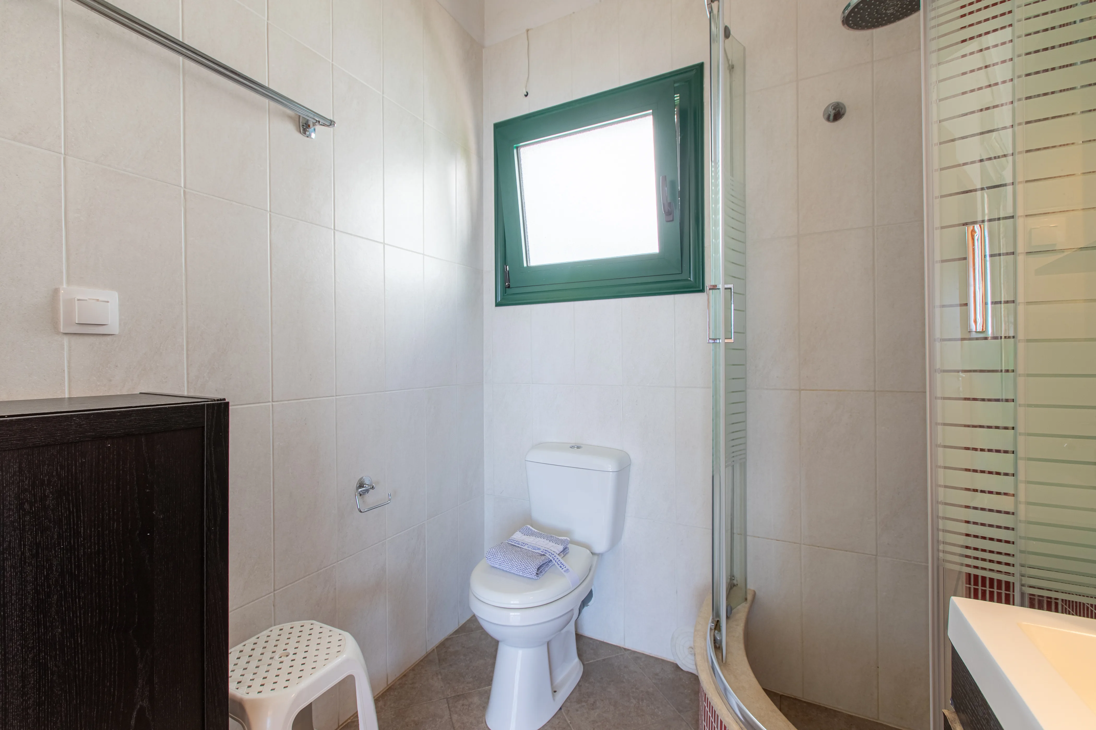 inside view of the apartment room bathroom with a toilet , a window above it and a shower area next to it