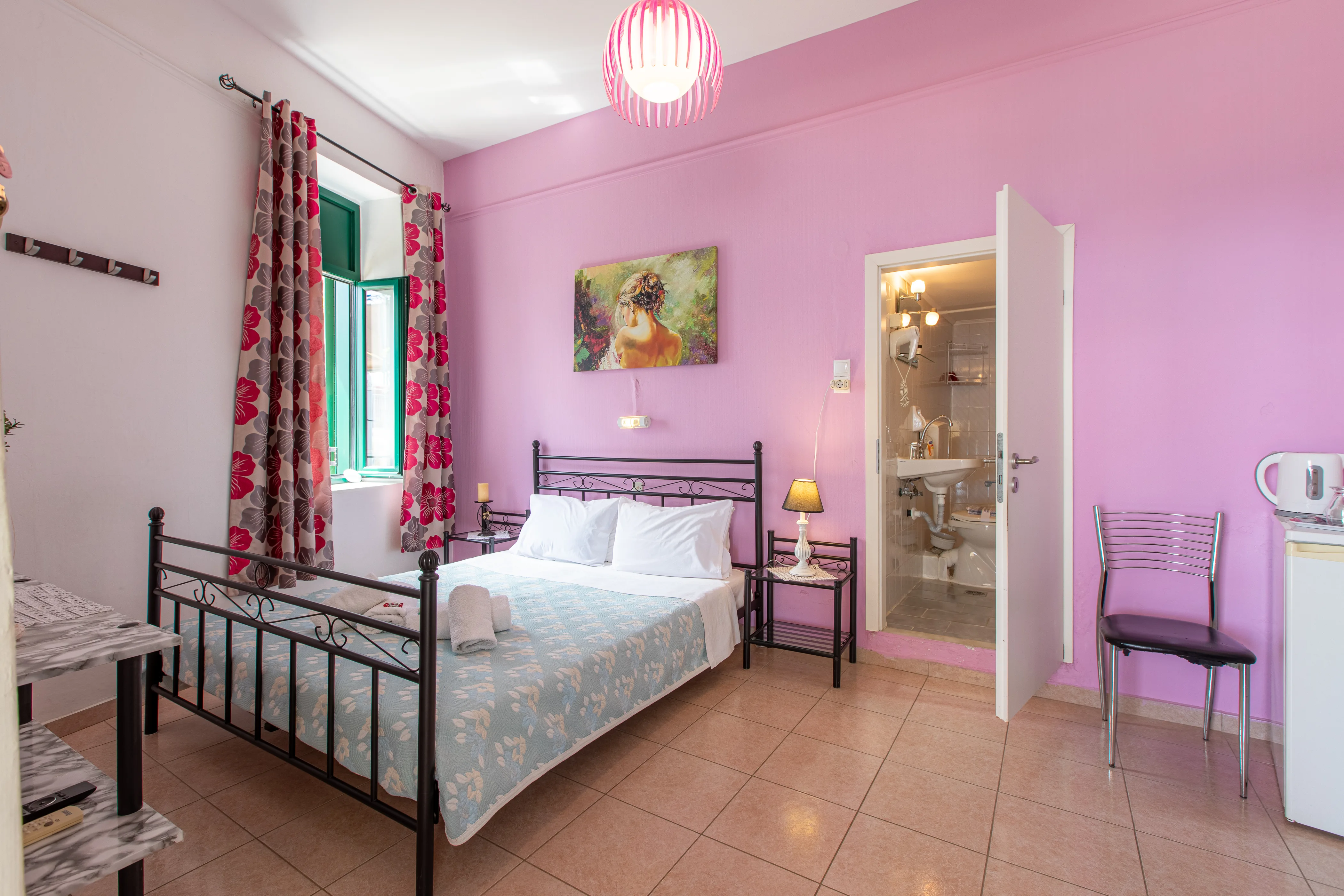 whole view of the double room with a large double bed, a window and a door leading to the bathroom in the back wall