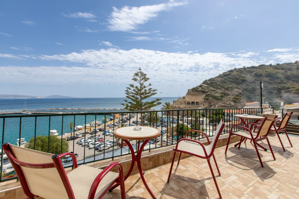 realistic view from the hotel balcony featuring some tables with armchairs and the sea at the background