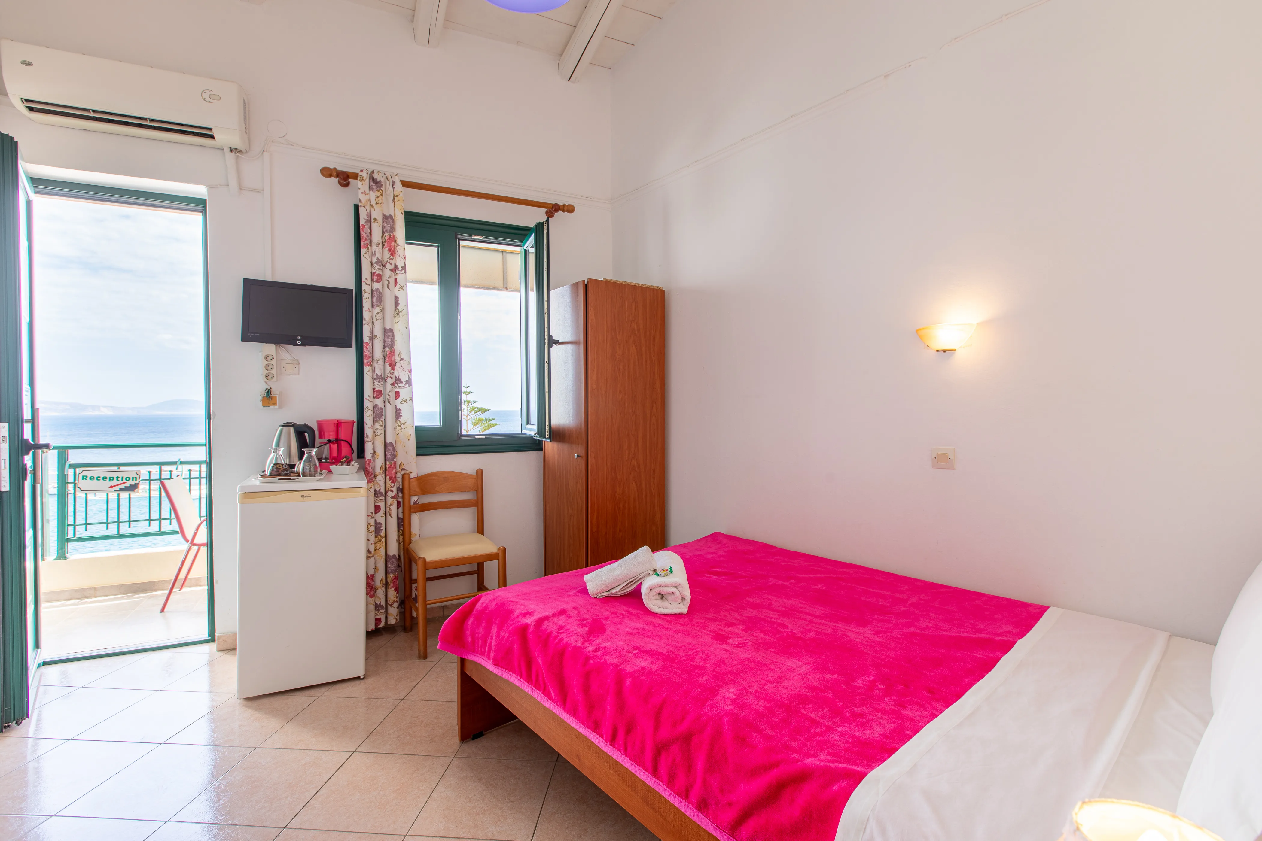 inside view of a room featuring a double bed with red bedsheets and view from the balcony in the background