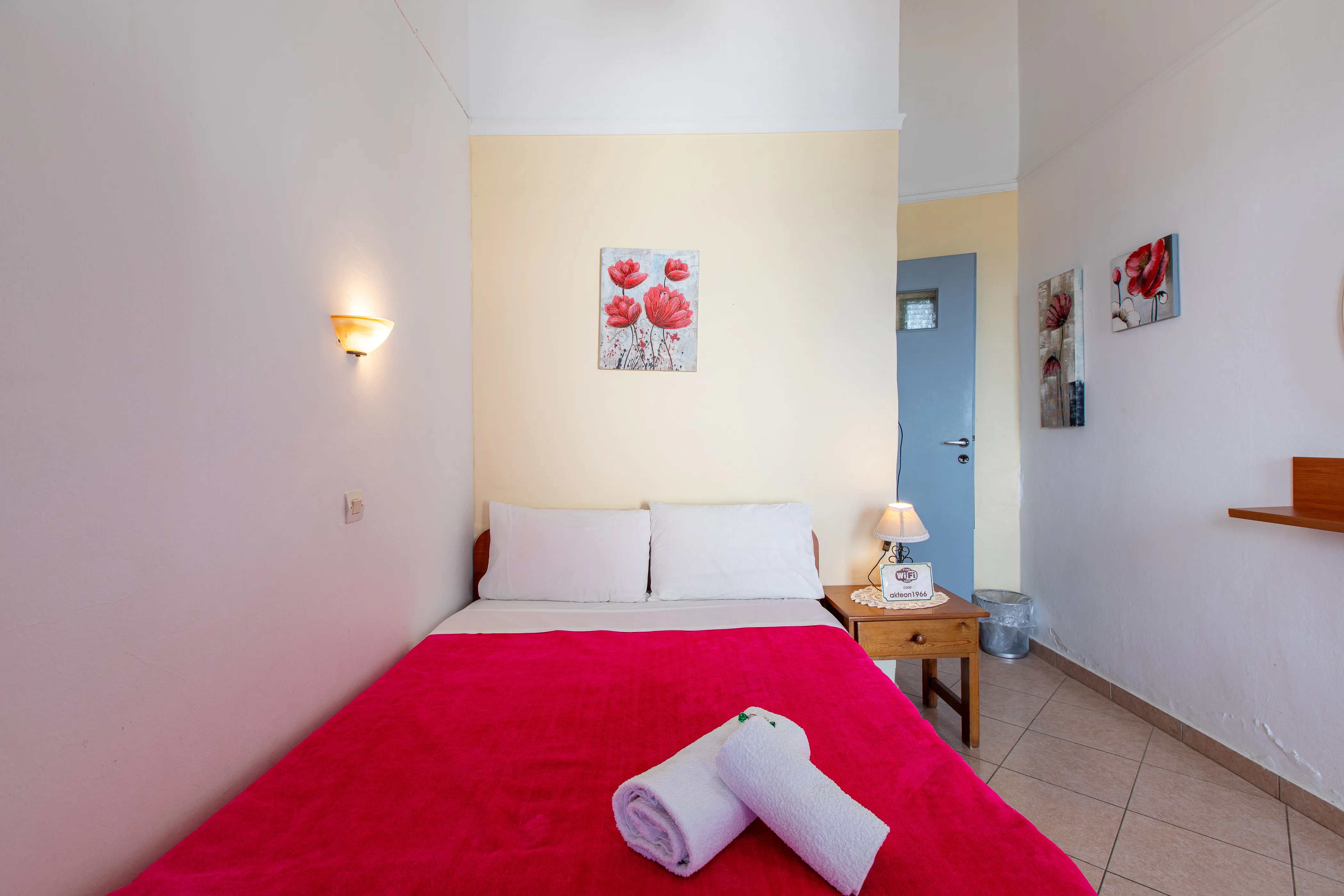 inside view of a room featuring a double bed with red bedsheets and a lot of flower paintings on the walls