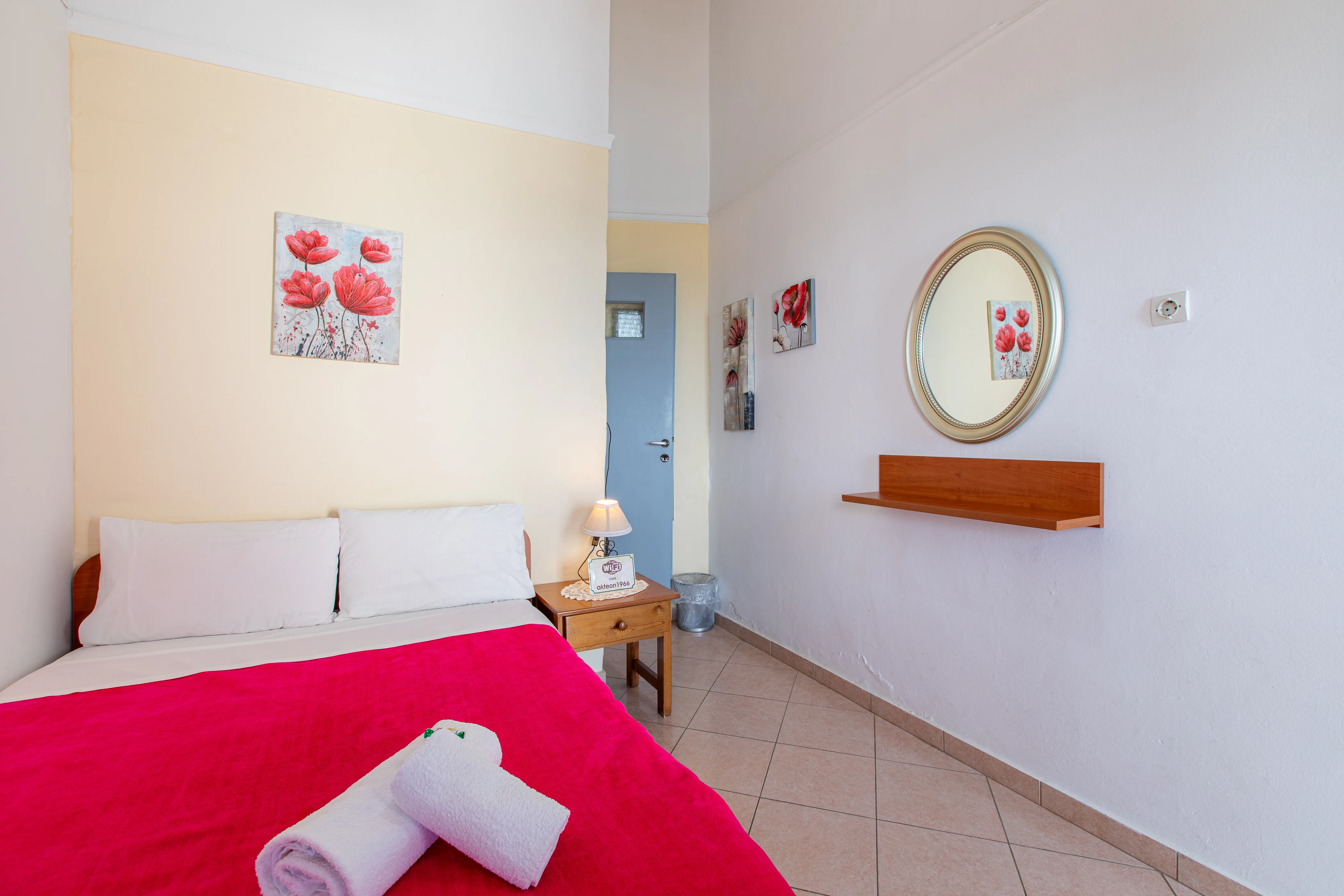 inside view of a room featuring a double bed with red bedsheets and a circular mirror on the side wall
