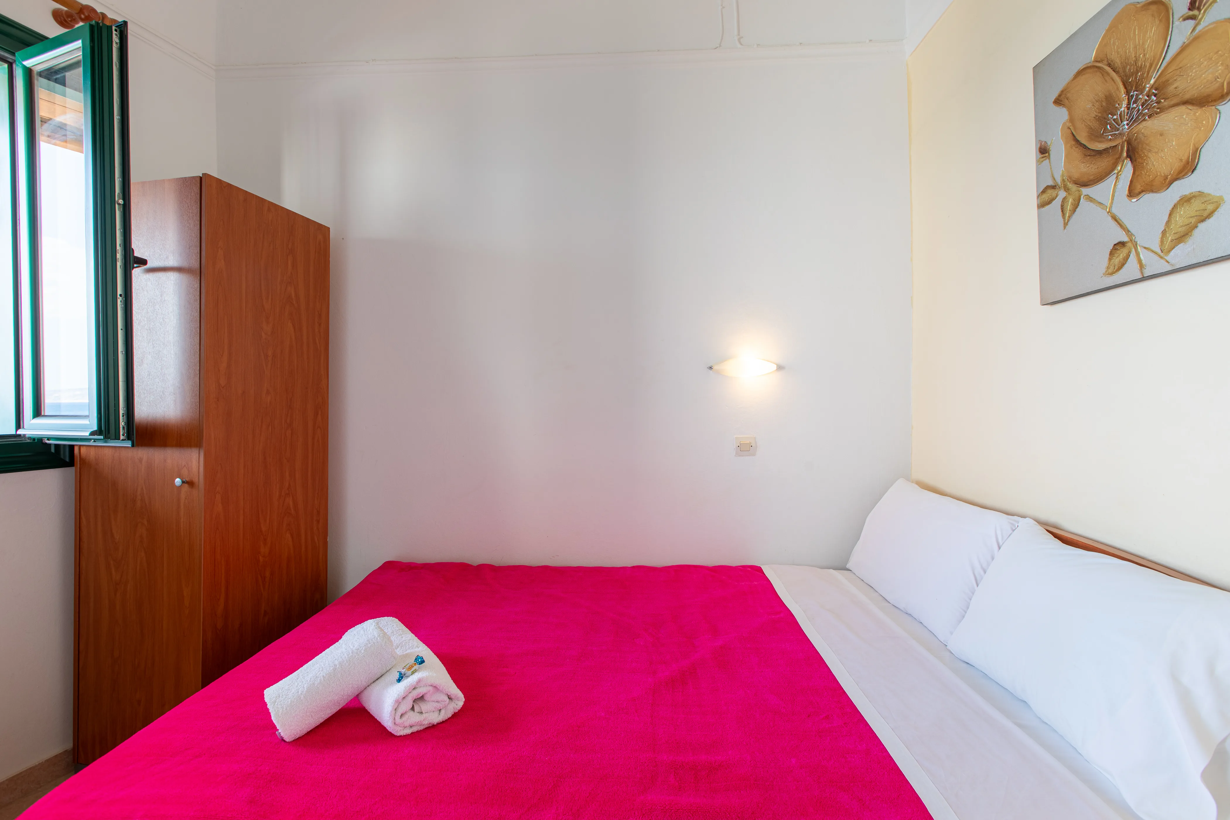 inside view of a room featuring a double bed with red bedsheets and a window in front of it