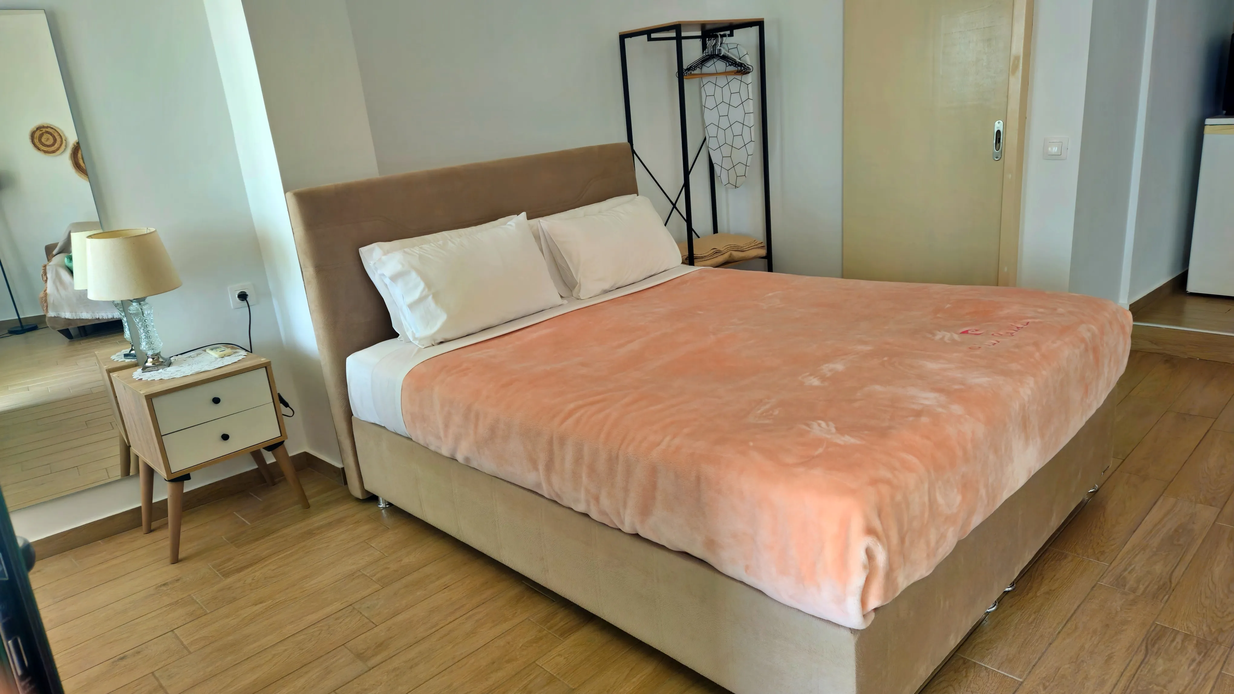 inside view of a hotel room featuring a large double bed from the side and nightstand next to it