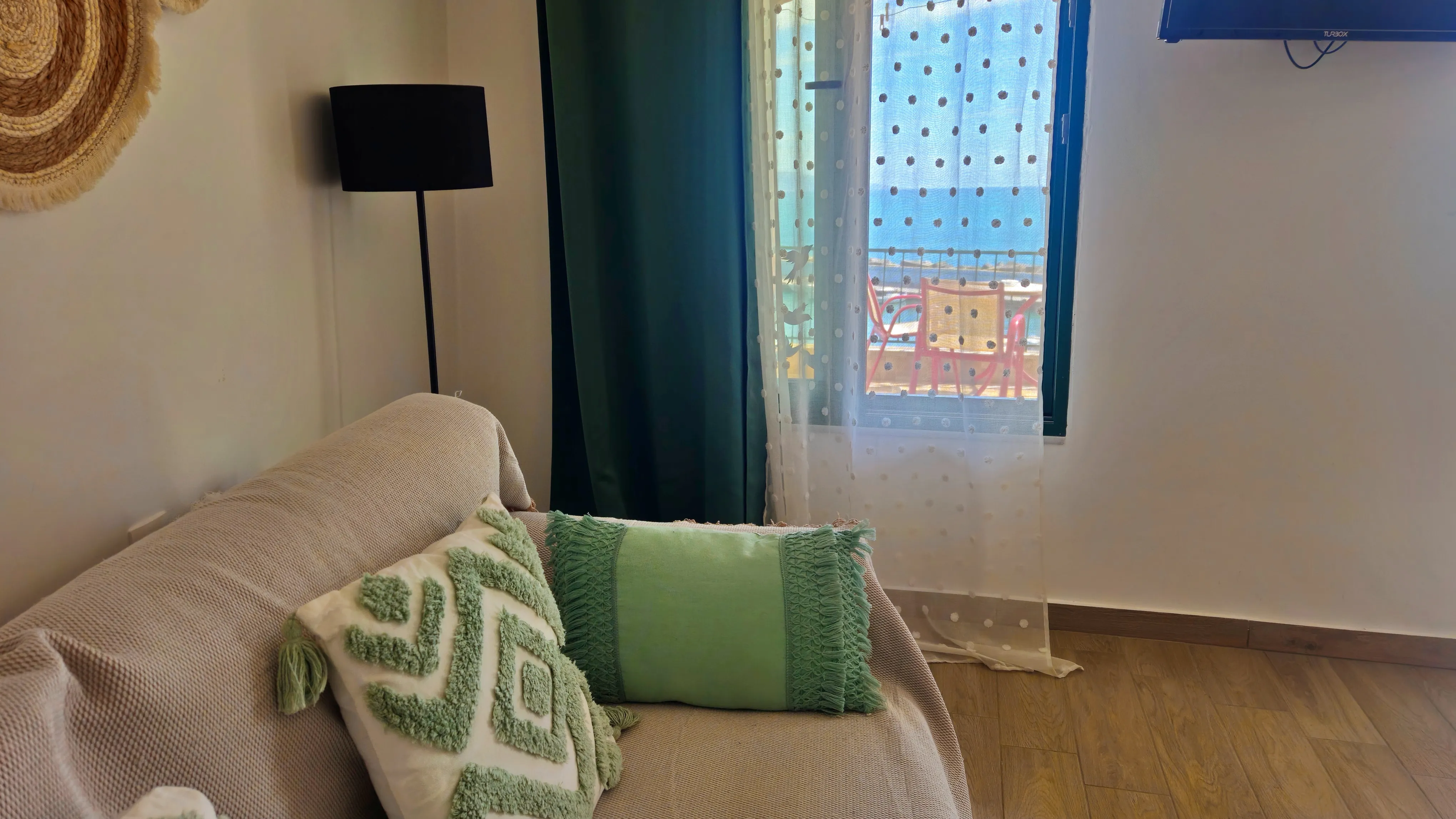inside view of a hotel room featuring a sofa from the side and a window looking at the sea in the background
