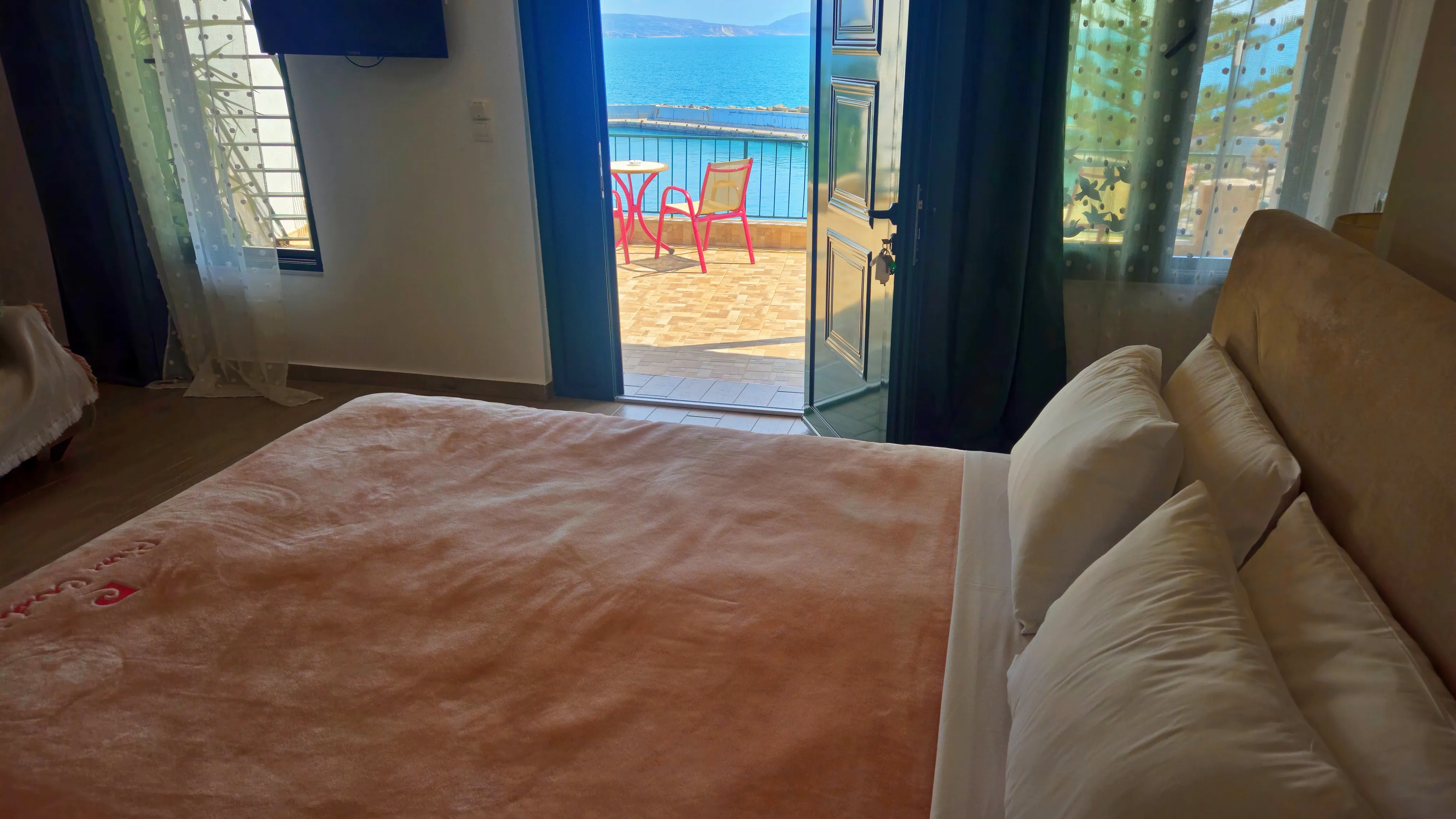 inside view of a hotel room featuring a large double bed and open door at the background that leads to the balcony