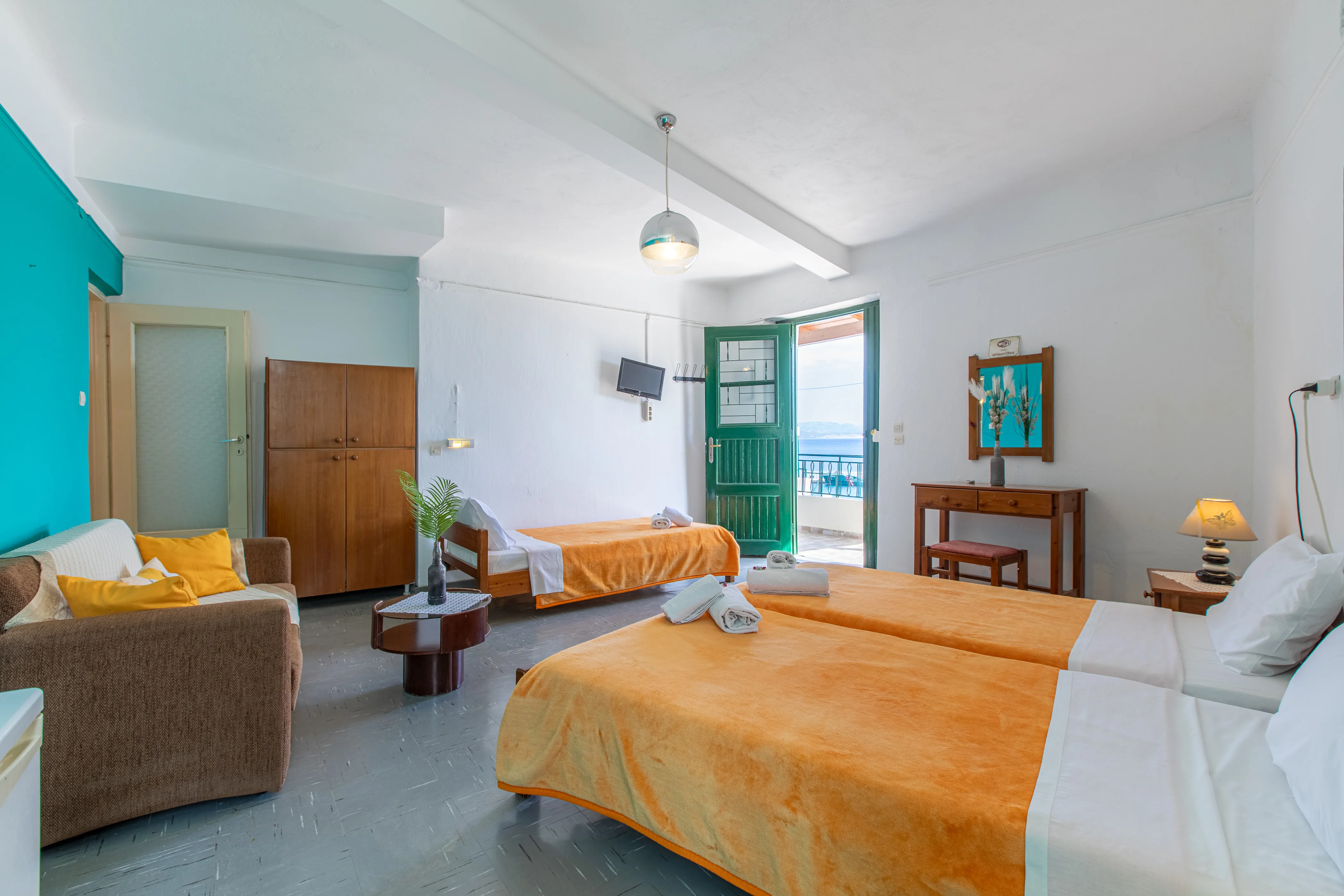 inside view of a room featuring two single beds on the right and another bed in the background next to the balcony door